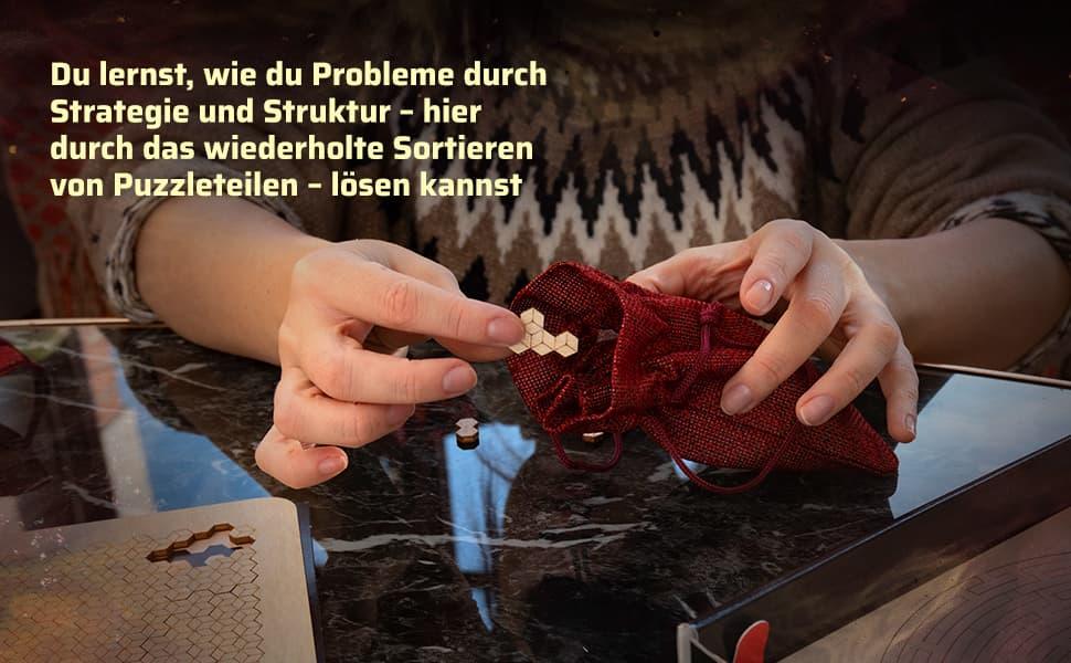 Nahaufnahme von Händen, die ein hexagonales Holzteilsortieren und in einen roten Stoffbeutel legen, mit Text zu Strategie und Struktur.