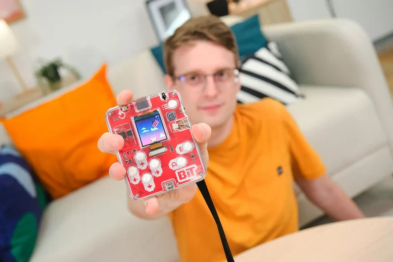 Person hält die fertig gebaute CircuitMess Bit 2.0 Retro-Konsole mit Umhängeband in die Kamera