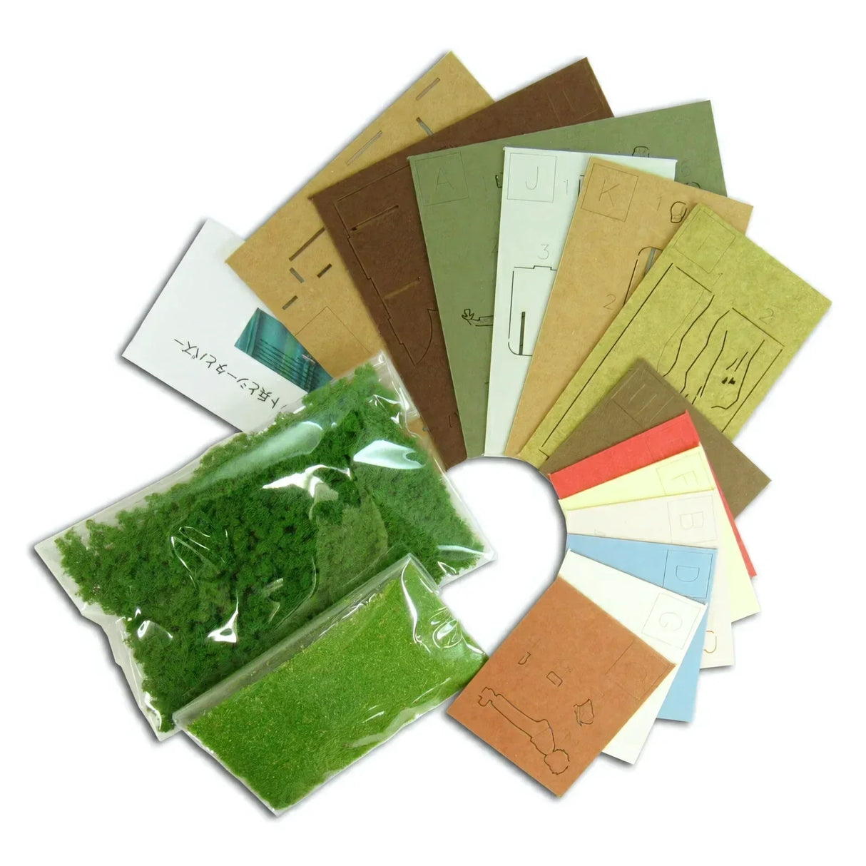 Modellbausatz mit grünen Streumaterialien und farbigen Kartonbögen