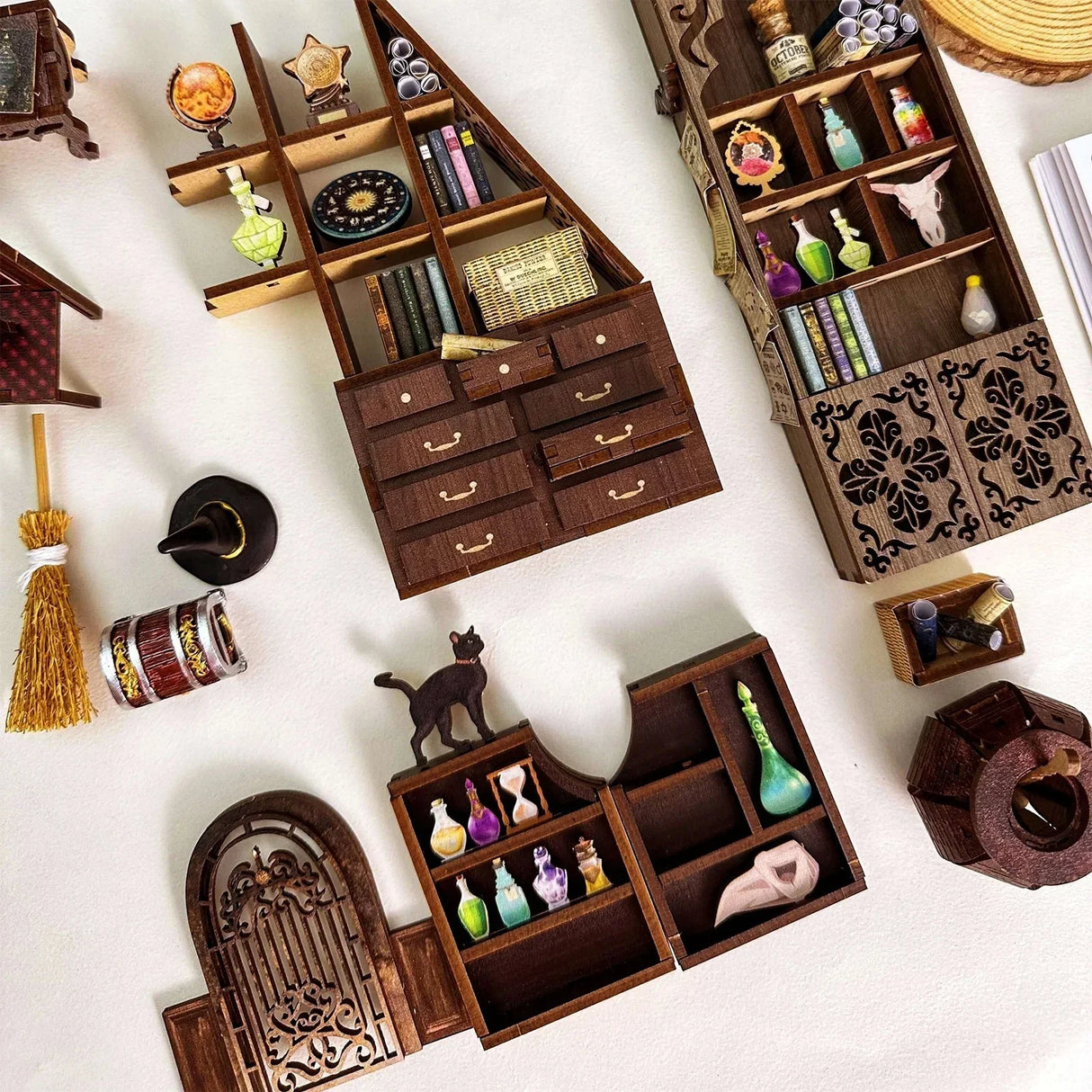 Drei Miniatur-Regale mit Tränken, Büchern und magischen Gegenständen, daneben ein Besen und ein Hexenhut
