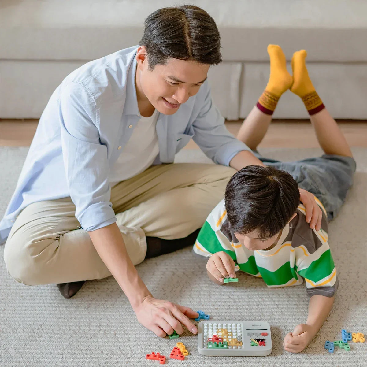 Vater und Sohn spielen auf dem Teppich ein Brettspiel mit bunten Formen