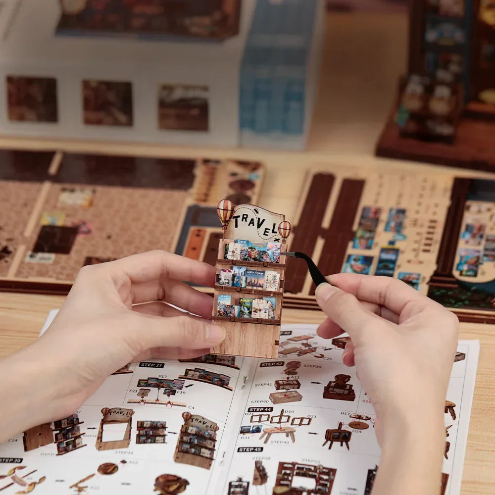 Hände bauen ein Miniatur-Reise-Bücherregal mit Pinzette und Anleitung