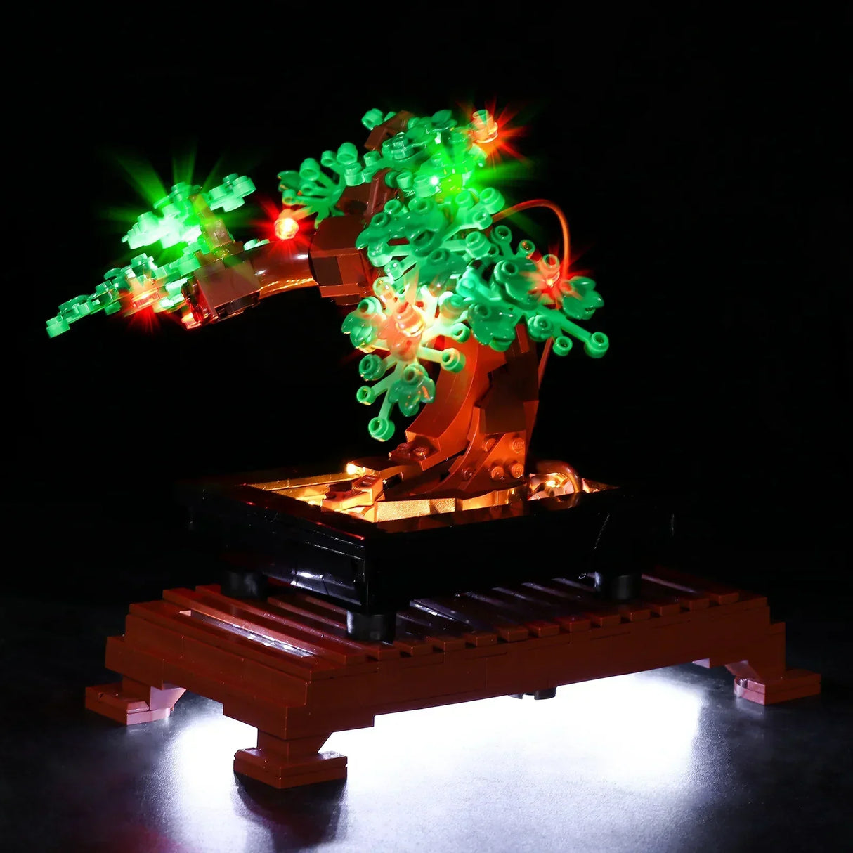 Eine leicht von unten fotografierte Ansicht des LEGO Bonsai-Baums. Die Kameraperspektive betont die Unterseite der Blätter und die Struktur des Stammes. Die warmweißen LEDs in der Schale leuchten die Unterseite des grünen Blätterdachs golden aus, ergänzt durch die strahlenden roten und grünen Lichtpunkte.