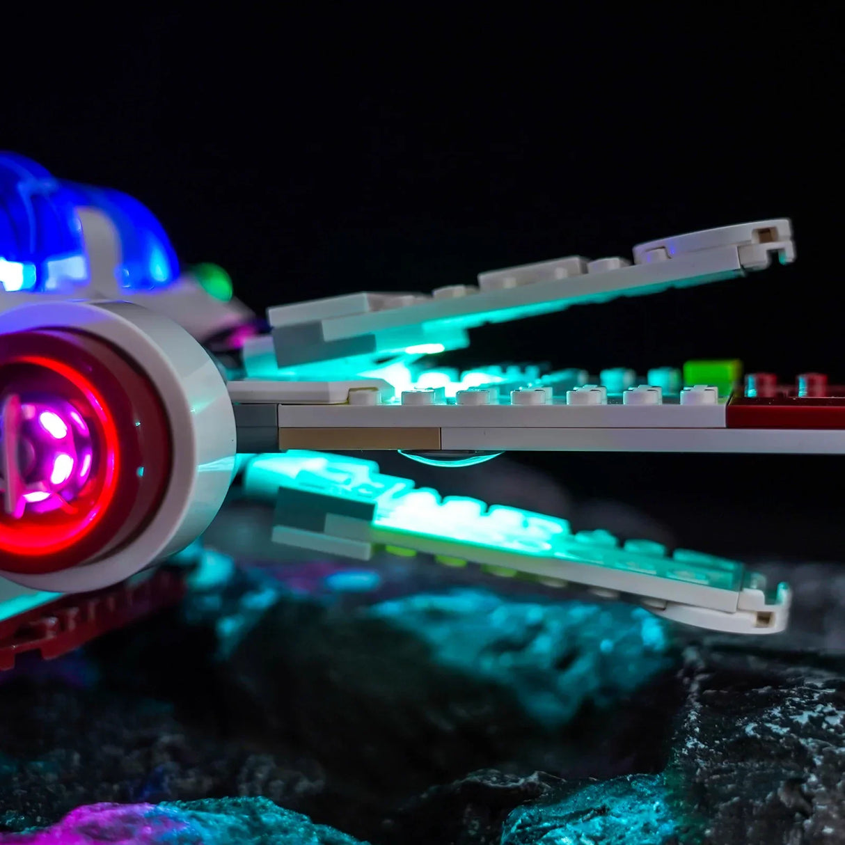 Nahaufnahme eines beleuchteten Lego-Raumschiffs mit roten, blauen und türkisen Lichtern auf dunklem Hintergrund