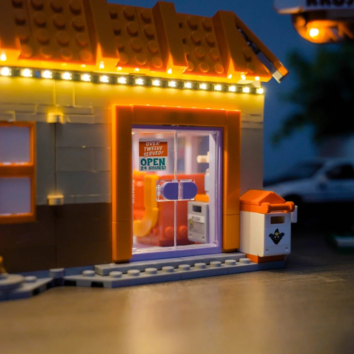 Nahaufnahme eines beleuchteten Lego-Gebäudes mit einem "Open 24 Hours"-Schild an der Tür
