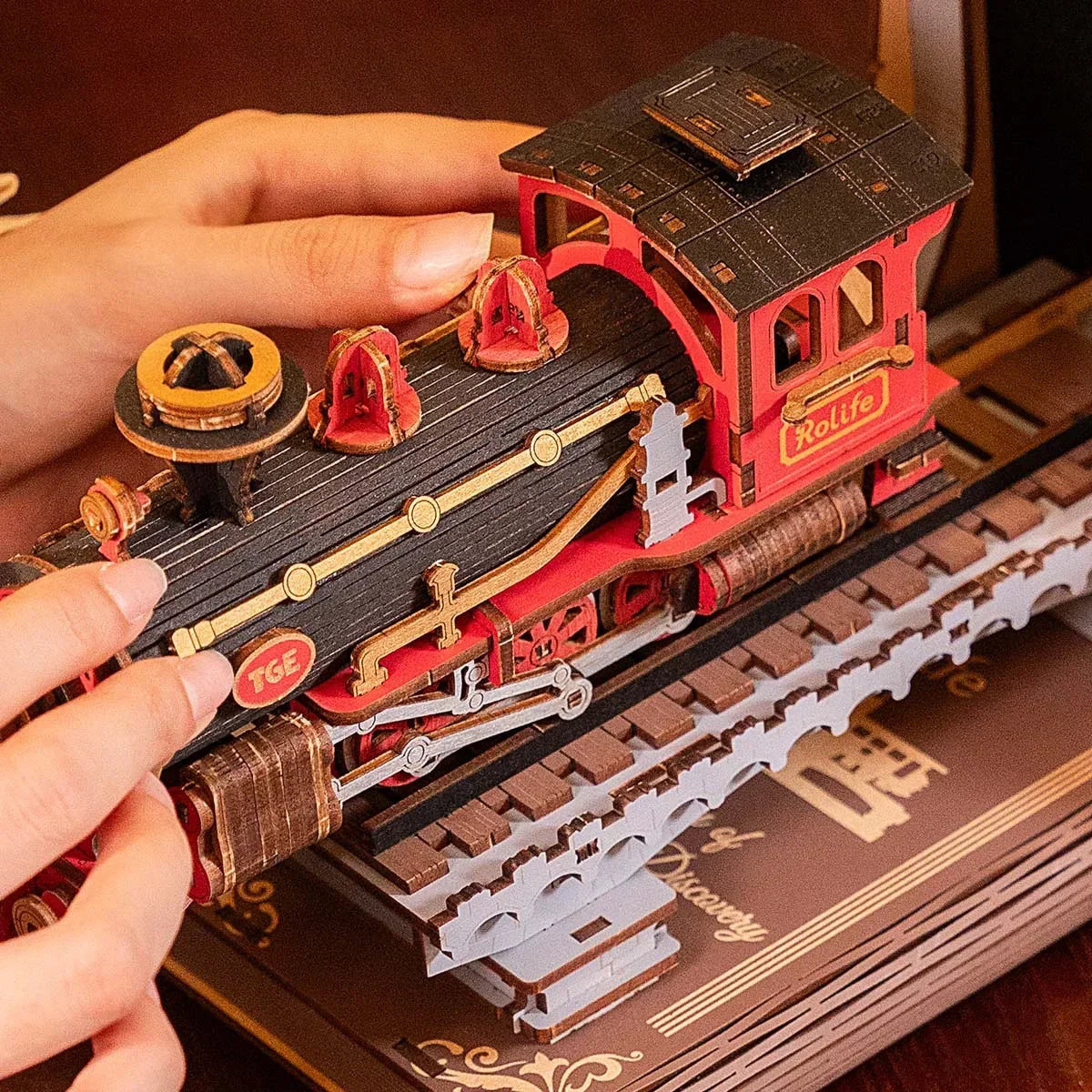 Hände halten ein rotes und schwarzes Holzmodell einer Dampflokomotive auf einem Gleis