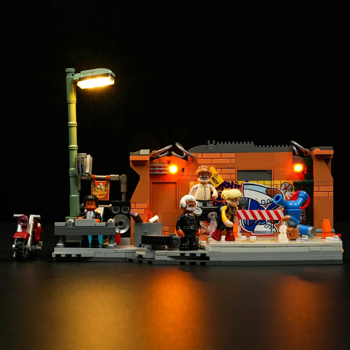 Lego-Szene mit beleuchteter Laterne, DJ, Motorrad und Figuren vor einer Backsteinwand mit Graffiti